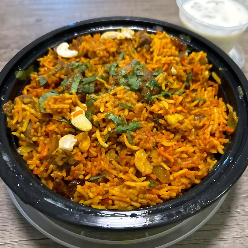 Close-up of Indian lamb biryani with cashews and cilantro, served with raita.