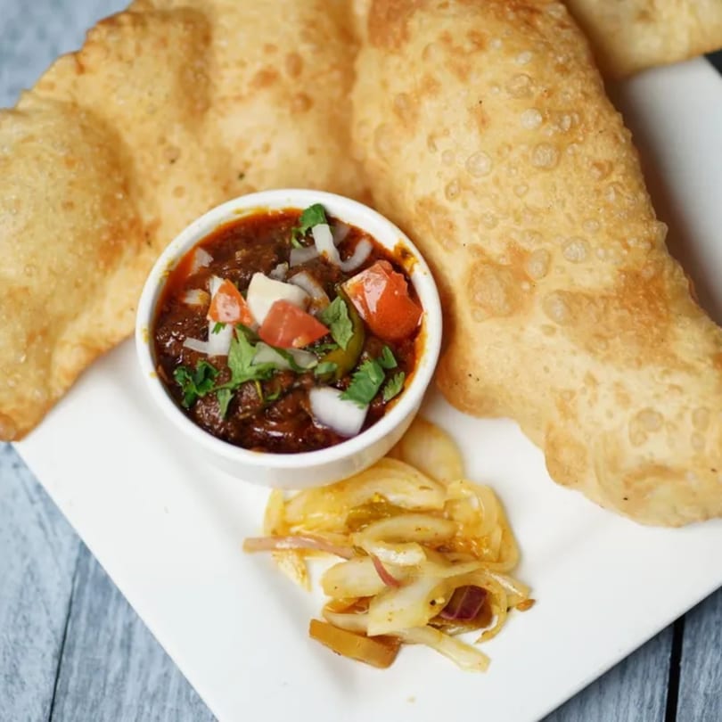Two golden-brown fried Indian breads with a bowl of chana masala and pickled onions.