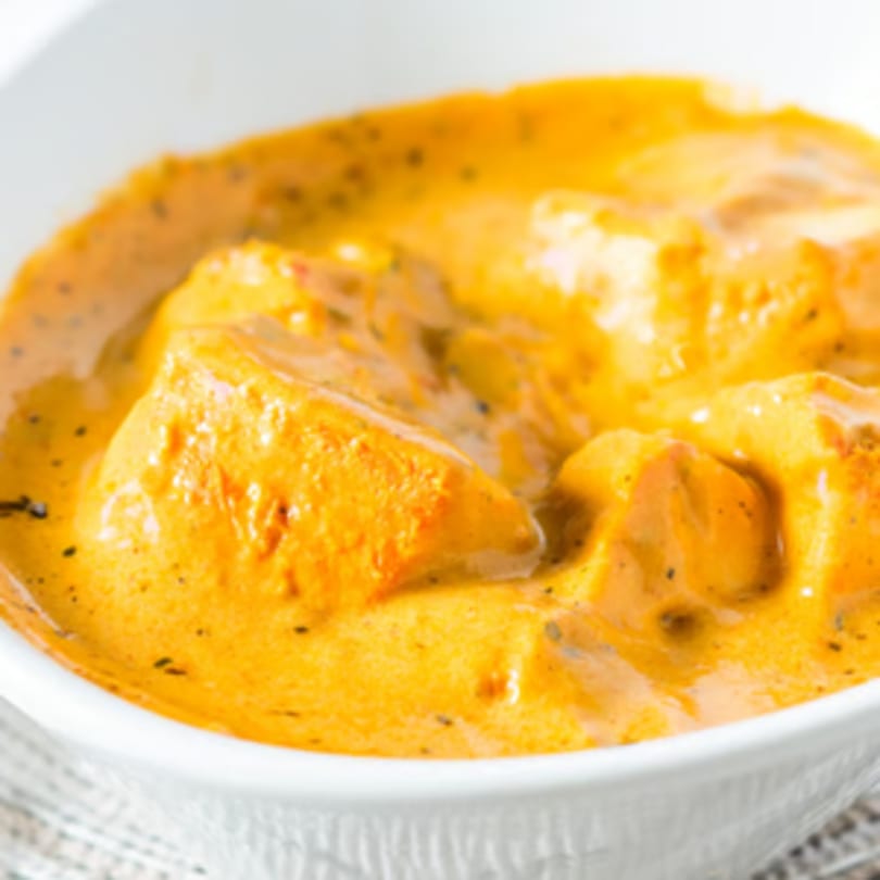 Close-up of creamy orange Indian curry with paneer cheese in a white bowl.