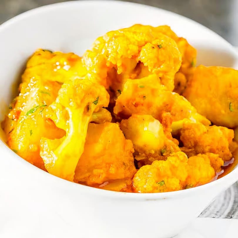 Close-up of Gobi Manchurian, a vibrant orange Indian cauliflower dish, in a white bowl.